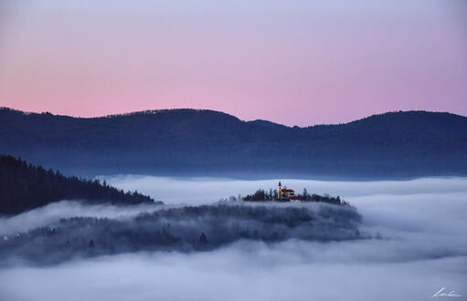 A bigger church rising from the morning fog (photograph).